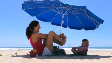 母亲和孩子在海滩上的蓝色阳伞下玩耍